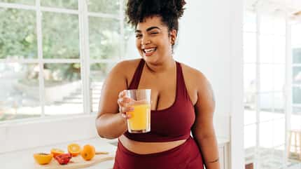 Lachende Frau hält Smoothie in die Kamera