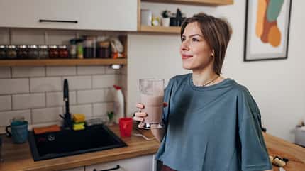 Beautiful fit woman drinking milkshake while standing in kitchen Beautiful fit woman drinking milkshake while standing in kitchen