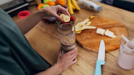 Close-up of woman's hands putting chopped banana in blender Close-up of woman's hands putting chopped banana in blender