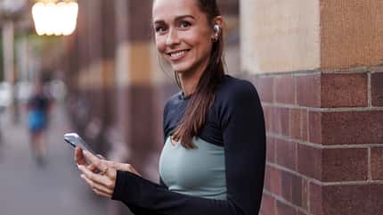 Eine Frau, die ihr Handy in der Hand hält und in die Kamera lächelt