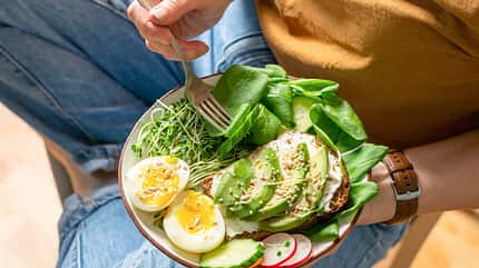 A woman holds a plate with useful healthy foods avocado, cucumber, spinach, radish, egg, microgreens