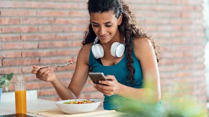 Junge Frau isst Salat und schaut auf ihr Handy Junge Frau isst Salat und schaut auf ihr Handy