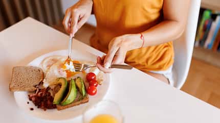 Frau schneidet Brot mit Spiegeleiern und Avocado Frau schneidet Brot mit Spiegeleiern und Avocado