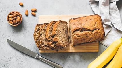 Aufgeschnittenes Bananenbrot mit Nüssen im Hintergrund und einem Schneidemesser