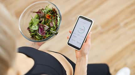 Eine Frau hält einen Salat und trackt Kalorien Eine Frau hält einen Salat und trackt Kalorien