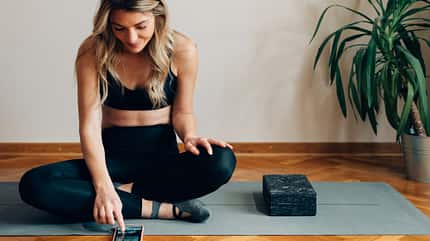 Eine Frau sitzt auf einer Yogamatte in Sportkleidung und schaut auf ihr Smartphone Eine Frau sitzt auf einer Yogamatte in Sportkleidung und schaut auf ihr Smartphone