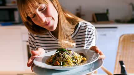 Eine Frau hält einen Teller mit Pasta in die Kamera