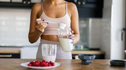 Frau in Sportkleidung bereitet einen Proteinshake zu Frau in Sportkleidung bereitet einen Proteinshake zu