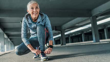 Eine ältere Dame in Sportkleidung schnürt sich die Sportschuhe zu