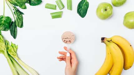 Hand, die Scoop mit Proteinpulver hält und darum Gemüse und Obst Hand, die Scoop mit Proteinpulver hält und darum Gemüse und Obst