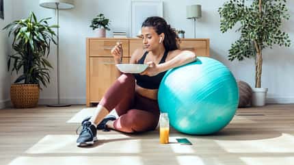 Frau sitzt an einem Gymnastikball und isst Frau sitzt an einem Gymnastikball und isst
