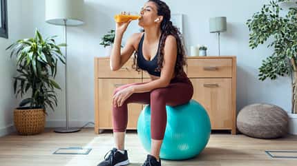 Frau sitzt auf Gymnastikball und trinkt gesunden Saft Frau sitzt auf Gymnastikball und trinkt gesunden Saft