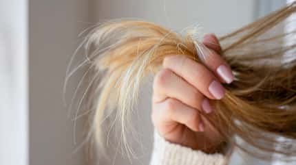 Eine Frau hält blonde Haarspitzen zwischen den Fingern
