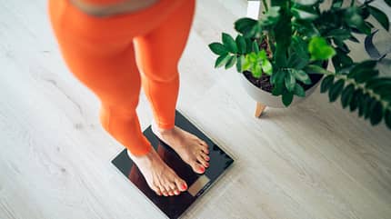Eine Frau in orangener Sportkleidung steht auf einer Waage Eine Frau in orangener Sportkleidung steht auf einer Waage