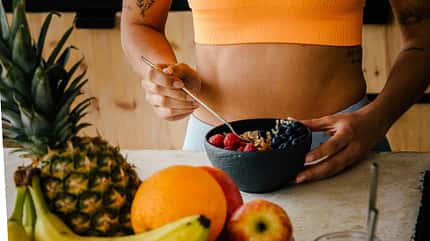 Frau in orangenem Sport-Bh hält eine Schale mit Obst Frau in orangenem Sport-Bh hält eine Schale mit Obst