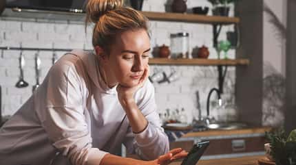 Eine Frau schaut beim Kochen auf ihr Smartphone Eine Frau schaut beim Kochen auf ihr Smartphone