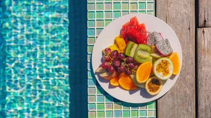 Teller mit verschiedenem Obst und Wasser im Pool im Hintergrund Teller mit verschiedenem Obst und Wasser im Pool im Hintergrund