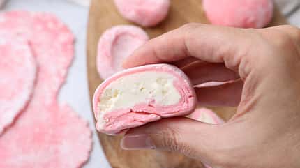 Eine Frau hält einen aufgeschnittenen rosanen Mochi in der Hand