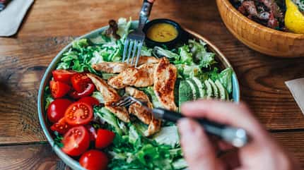 Eine Frau schneidet einen Caesar-Salad