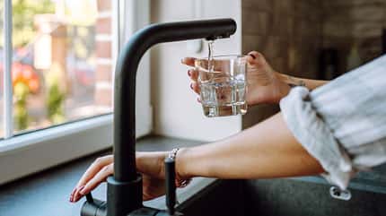 Eine Frau hält ein Glas unter den Wasserhahn Eine Frau hält ein Glas unter den Wasserhahn