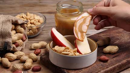 Eine Frau taucht ein Stück Apfel in Erdnussbutter Eine Frau taucht ein Stück Apfel in Erdnussbutter