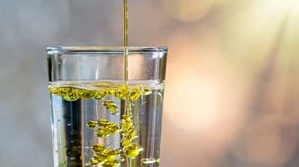 Olivenöl wird in ein Wasserglas gegossen Olivenöl wird in ein Wasserglas gegossen