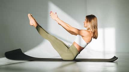 Eine Frau macht die Boot-Position auf einer Yogamatte Eine Frau macht die Boot-Position auf einer Yogamatte