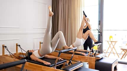 Frauen dehnen sich an Reformer-Pilates-Geräten Frauen dehnen sich an Reformer-Pilates-Geräten