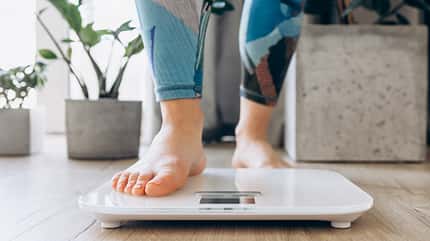 Weibliche Füße, die auf eine Waage steigen Weibliche Füße, die auf eine Waage steigen