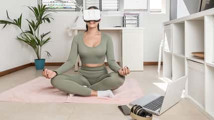 Eine Frau sitzt im Schneidersitz auf einer Yogamatte mit einer VR-Brille auf 