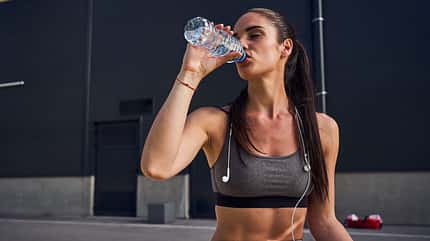 Dehydrated female runner drinking a water so she can refresh for another round of running Dehydrated female runner drinking a water so she can refresh for another round of running