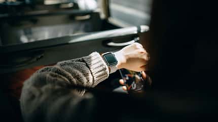 Over the shoulder view of young Asian woman holding smartphone and checking time on smartwatch while commuting in the city riding on a minibus Over the shoulder view of young Asian woman holding smartphone and checking time on smartwatch while commuting in the city riding on a minibus