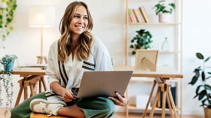 Eine Frau sitzt im Schneidersitz mit ihrem Laptop auf den Knien Eine Frau sitzt im Schneidersitz mit ihrem Laptop auf den Knien