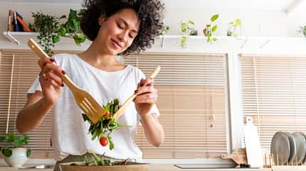 Happy young multiracial woman mixing bowl of fresh salad. Copy space.Healthy lifestyle
