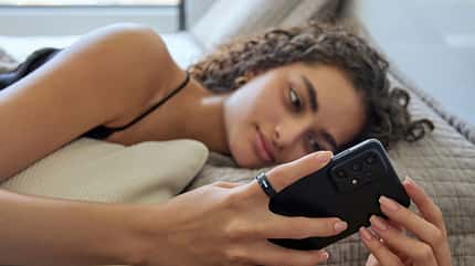 Eine Frau liegt im Bett und schaut auf ihr Smartphone Eine Frau liegt im Bett und schaut auf ihr Smartphone