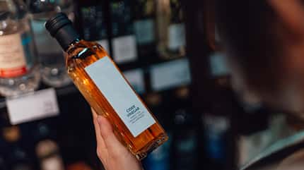 Eine weibliche Hand, die im Supermarkt eine Flasche Apfelessig hält Eine weibliche Hand, die im Supermarkt eine Flasche Apfelessig hält