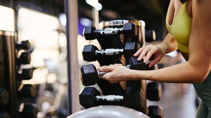 Athletic woman taking dumbbell from rack in gym Athletic woman taking dumbbell from rack in gym