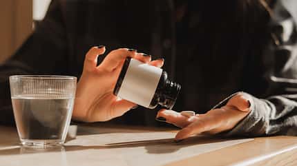 Careful Dose: Woman Drops Vitamin Pill From Bottle Onto Hand With Glass of Water Nearby Careful Dose: Woman Drops Vitamin Pill From Bottle Onto Hand With Glass of Water Nearby