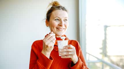smiling woman in a cozy sweater eats homemade yogurt with granola, basking in the morning sunlight by the window. smiling woman in a cozy sweater eats homemade yogurt with granola, basking in the morning sunlight by the window.