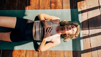 Directly above shot of woman lying down on yoga mat with hands on chest at wellness resort