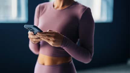 Frau in lavendelfarbener Sportkleidung schaut auf ihr Smartphone