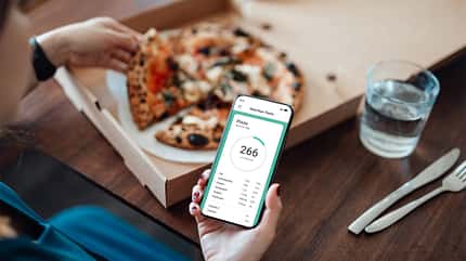 Junge Frau nutzt eine App, um Kalorien einer Takeaway-Pizza per Smartphone zu tracken