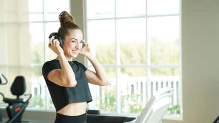 Frau lächelt auf dem Laufband im Fitnessstudio und setzt sich Kopfhörer auf. Frau lächelt auf dem Laufband im Fitnessstudio und setzt sich Kopfhörer auf.