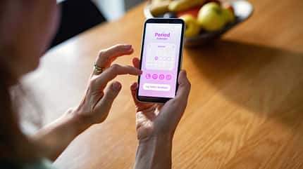 Frau nutzt auf dem Smartphone eine Perioden-Tracking-App mit Kalenderansicht.