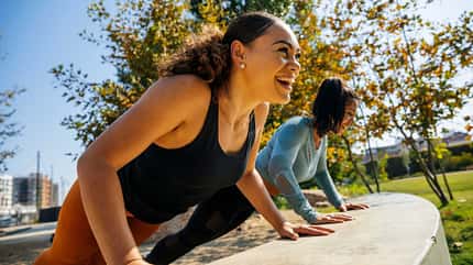 Lachende Frau macht mit anderen im Park Push-Ups an einer Mauer