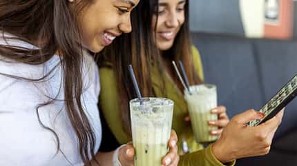 Zwei Mädchen mit einem Glas Matcha in der Hand schauen auf ein Smartphone