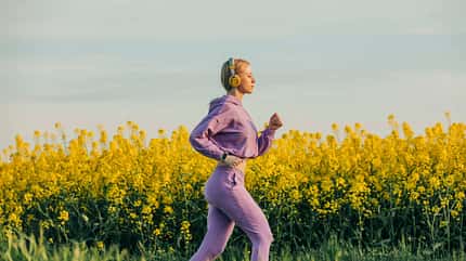 Frau joggt mit Kopfhörern durch ein blühendes Rapsfeld.