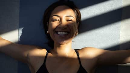 Topshot einer lächelnden Frau, die nach einem Workout in der Sonne auf einer Yogamatte liegt