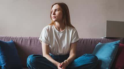 Frau sitzt im Schneidersitz auf dem Sofa und schaut in die Ferne