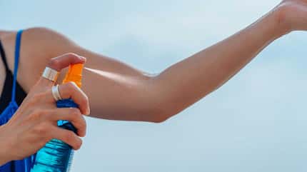 Der Arm einer Frau wird mit Sonnencreme eingesprüht